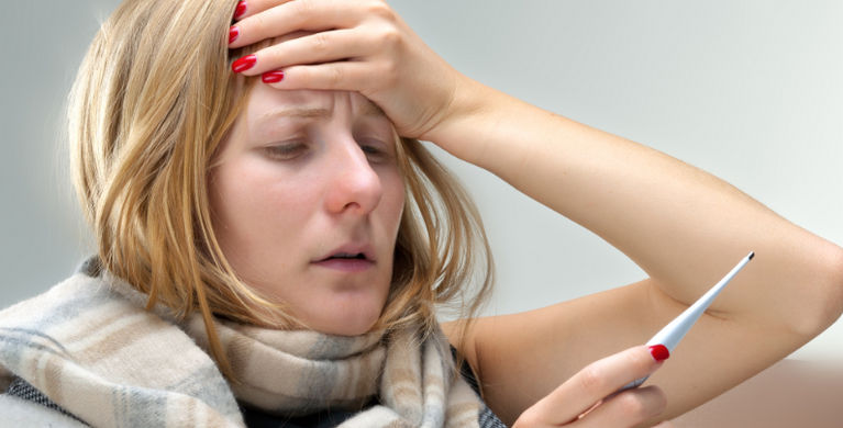 женщина смотрит на градусник и приложила руку ко лбу